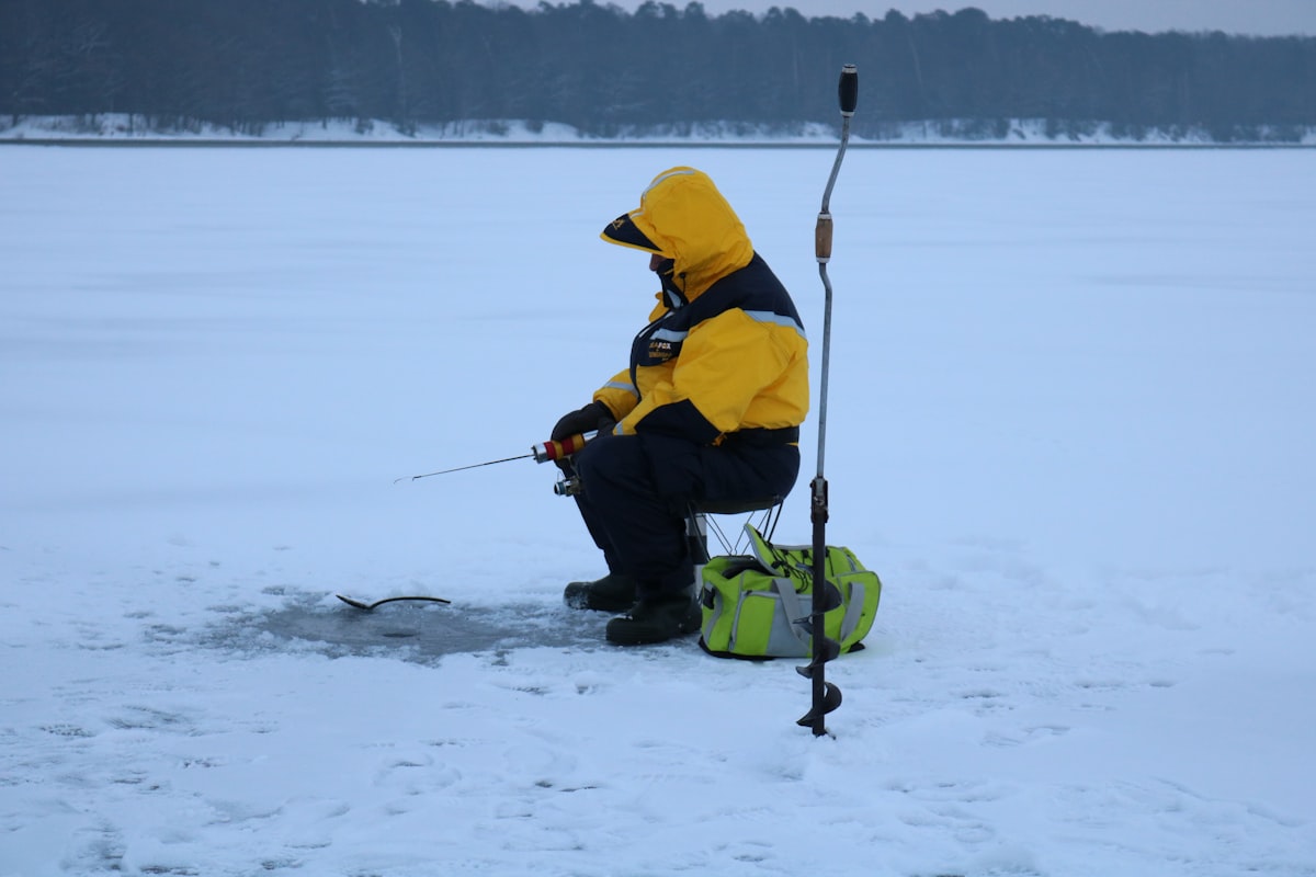 A person fishing on a frozen lake at sunrise