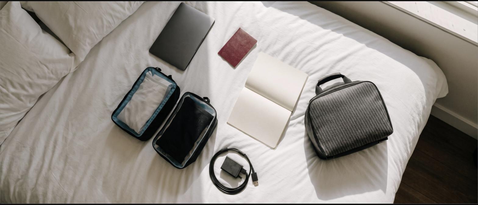Laptop, passport, packing cubes, charger and notebook laid out on a bed